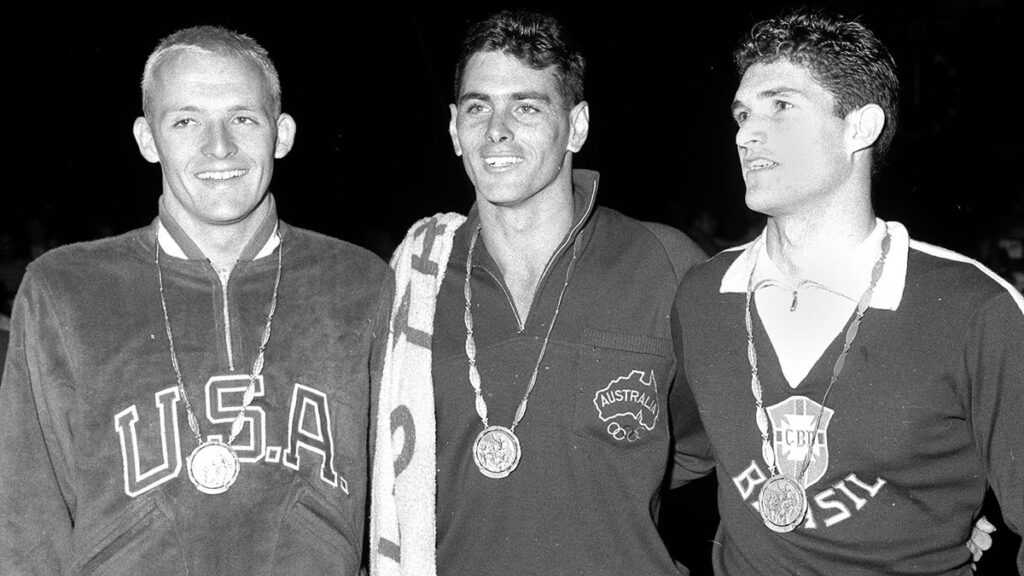 Lance Larson y el día que un juez le negó el oro olímpico en Roma 1960 La delegación de los Estados Unidos es conocida por destacar ampliamente en el deporte, dominio que queda clarificado ante los ojos del mundo en los Juegos Olímpicos. Una de las disciplinas que ha logrado dominar casi en su totalidad es la natación, con un sinnúmero de medallas en su poder. Lamentablemente, debido a decisiones polémicas, en los Juegos Olímpicos de Roma 1960 no pudieron escribir el nombre de Lance Larson a su larga lista de campeones. El nacido en California llegó a la justa olímpica con las credenciales para poder destacar en las pruebas acuáticas. Ganador de campeonatos en la NCAA y poseedor de récords mundiales, sin duda se esperaba que lograra aparecer en las finales. Larson cumplió con el pronóstico tras llegar a la final de los 100 metros estilo libre, misma en la que se encontró con otro gran favorito de la época: el medallista de plata en 1956, John Devitt. La prueba se desarrolló como se esperaba por los especialistas, al grado de que ambos acabaron la final al mismo tiempo. En aquel entonces, los sensores electrónicos no eran utilizados como parámetro para definir al ganador (aunque si existían), sino que cada carril contaba con tres jueces para estar atentos a los tiempos del atleta correspondiente. El momento culminante de la prueba no fue la prueba en sí, sino el momento en el que los jueces tardaron para determinar al ganador. Dos de los tres jueces encargados para definir al primer lugar decretaron que Devitt era el ganador de la medalla de oro, mientras que dos de tres encargados de definir al segundo lugar…vieron a Devitt como el ganador de la medalla de plata. Con las opiniones divididas de seis jueces, fue turno de conocer los tiempos de los denominados ‘cronómetros de respaldo’, mismos que marcaron para Larson tiempos de 55,0, 55,1 y 55,1, mientras que los de Devitt revelaron tres tiempos de 55,2. Dicha decisión, parecía darle la medalla de oro al estadounidense; sin embargo llegaría la inesperada decisión final del juez de la carrera, la del sueco Henry Runstromer. Sin evaluación alguna, le terminó dando la medalla de oro a Devitt. Larson y la delegación estadounidense no repararon en quejas, sobre todo por el hecho de que un juez, sin consultar elementos de apoyo determinó la victoria y derrota de los atletas en la final. Más allá de que la voz de los estadounidenses fuera escuchada, Runstromer determinó que los tiempos de Larson quedarían también en 55,2, esto con el fin de ‘justificar’ la decisión final. Lamentablemente, con todo en contra, Larson se tuvo que conformar y quedarse con la medalla de plata, detrás de Devitt y por delante del brasileño Manuel dos Santos. El premio de ‘consolación’ para Larson llegó en la final de los 4x100 combinados, en donde obtuvo la medalla de oro.